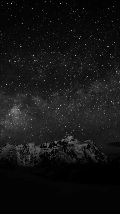 The Milky Way spreads in grainy monochrome above a jagged mountain ridge, the lower third left almost entirely dark.