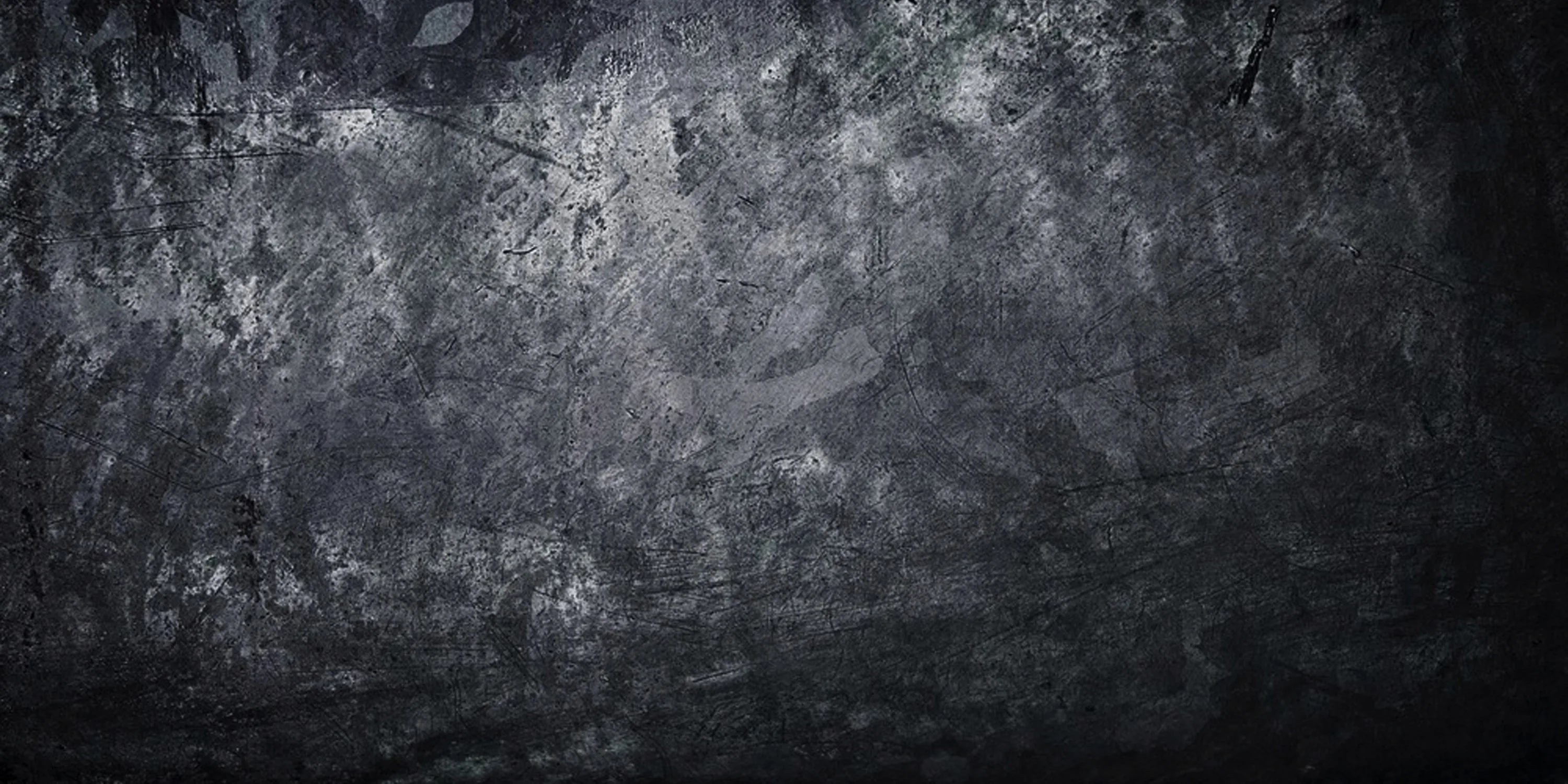 A mottled charcoal surface with scuffs and pale patches through the middle, darkening steadily toward all four corners.