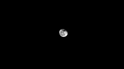 The moon sits just above centre in an empty black sky, craters showing along its lit lower edge and nothing else in the frame.