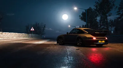 A classic 911 sits on a rain-slicked mountain road at night, a full moon and one streetlight throwing long reflections down the empty lane.