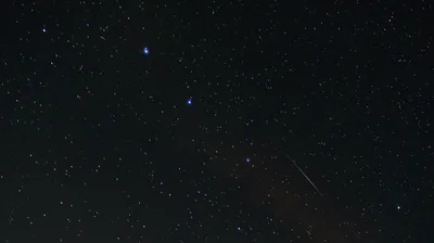 A thin trail cuts down toward the lower right of a dark blue sky, with the brighter stars gathered near the top of the frame.