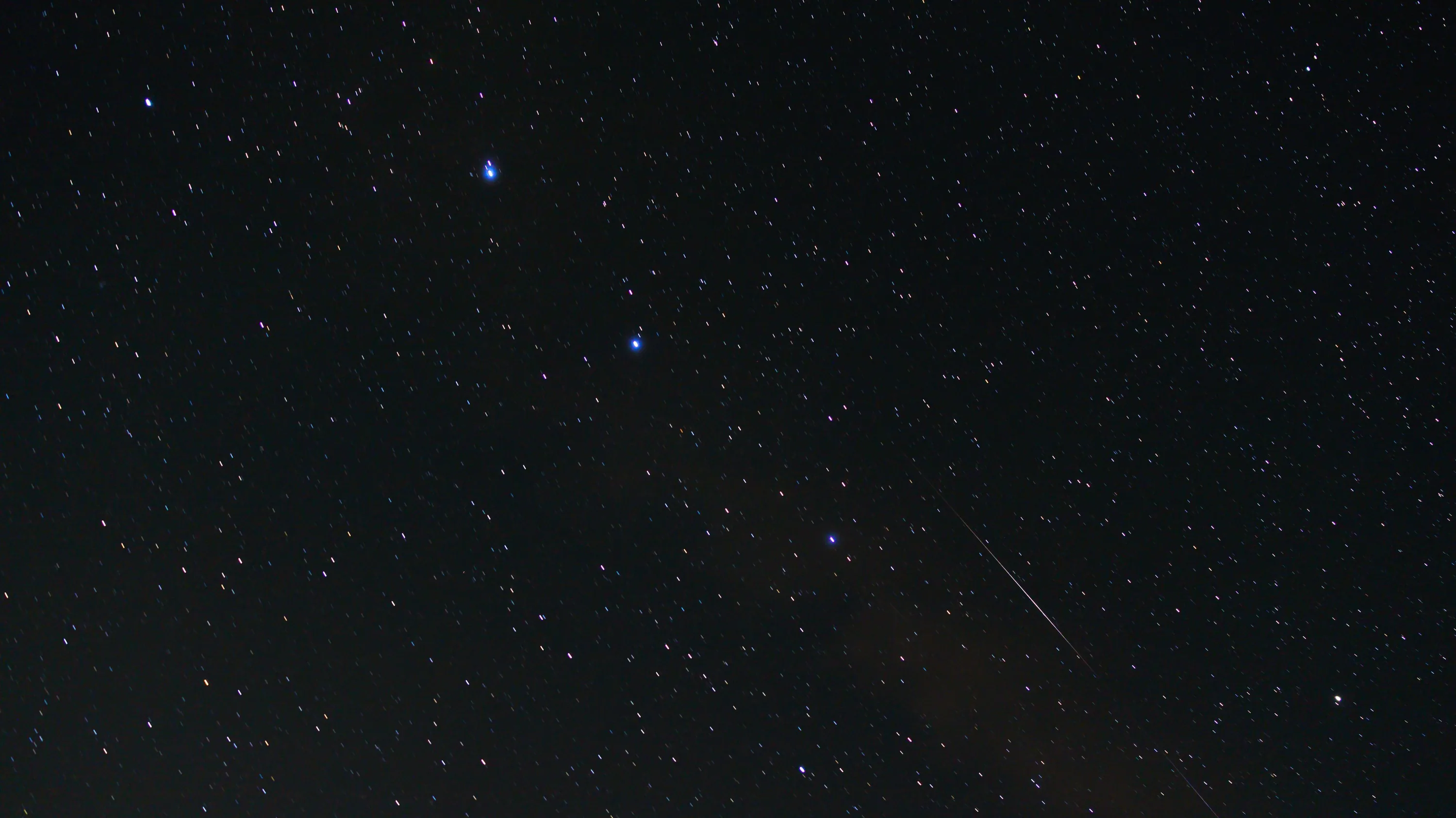 A thin trail cuts down toward the lower right of a dark blue sky, with the brighter stars gathered near the top of the frame.