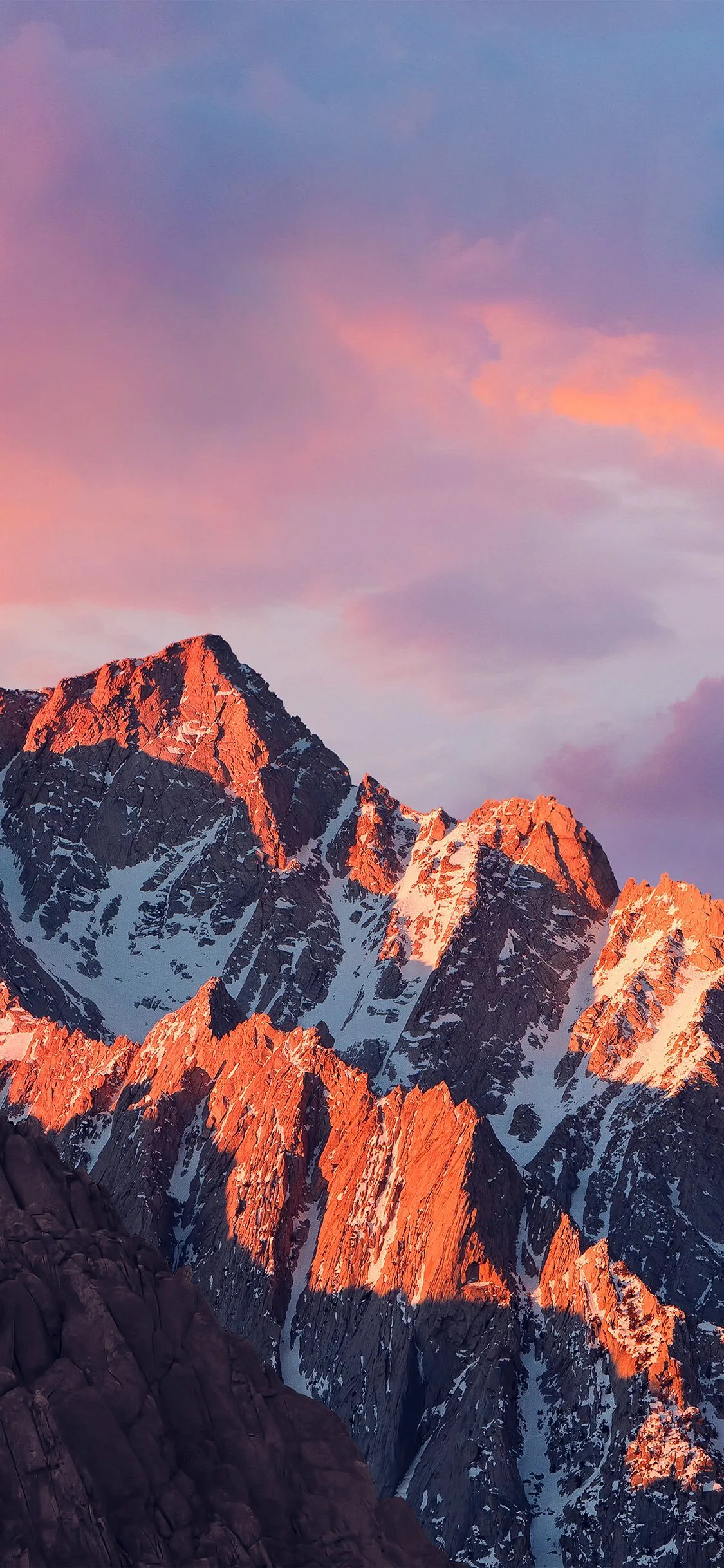 Pink alpenglow washes over craggy granite ridges beneath purple clouds, the shadowed lower slopes staying dark enough for the dock.