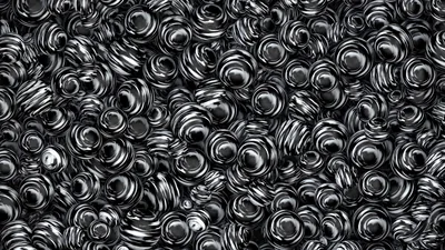 Hundreds of polished coiled forms pile on top of each other, each catching a bright highlight so the surface reads as liquid metal.