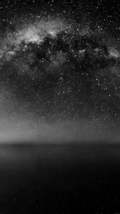 The Milky Way spreads across the top of the frame in black and white, a flat dark sea sitting quiet beneath the star field.